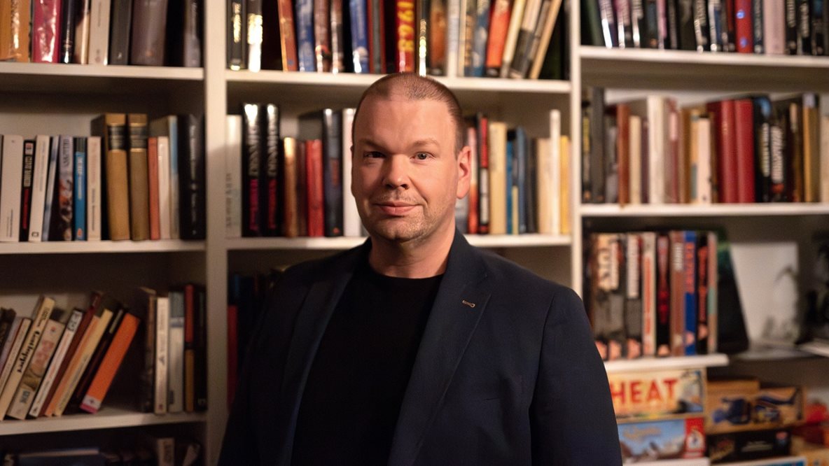 Författaren Emil Haskett framför en bokhylla fylld av böcker