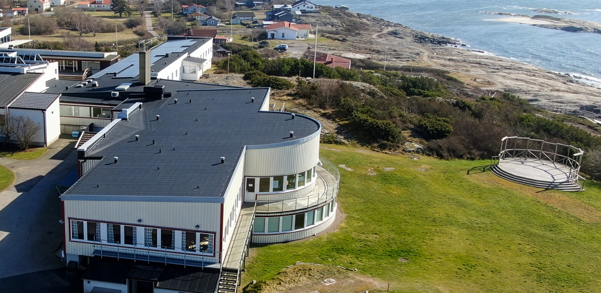 Flygbild över skolan vid kusten. Moderna byggnader, hav och bostäder i bakgrunden.