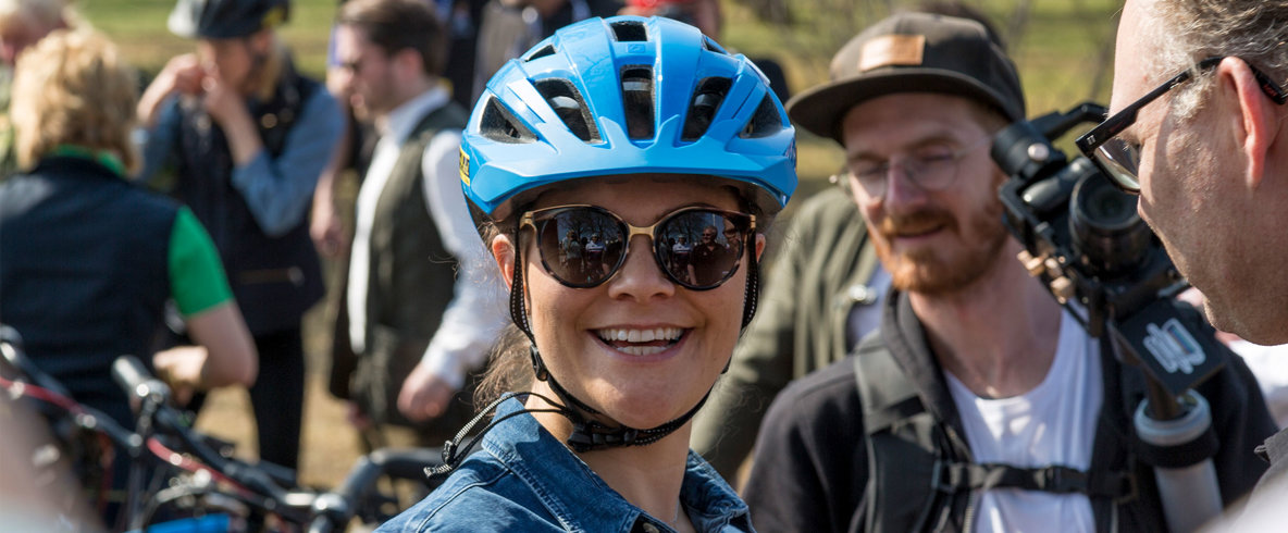 Kronprinsessan har tagit på sig en blå cykelhjälm och ler in i kameran.