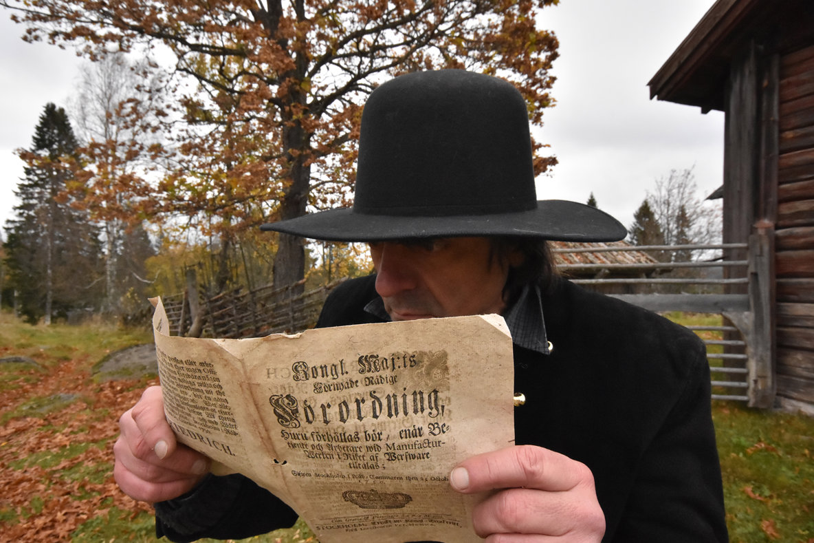 Foto på en man i ålderdomliga kläder som läser en tidning.