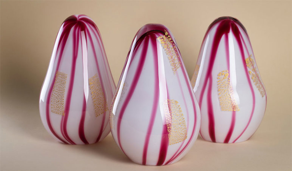 Tre vita glasskulpturer med detaljer i rött och guld.