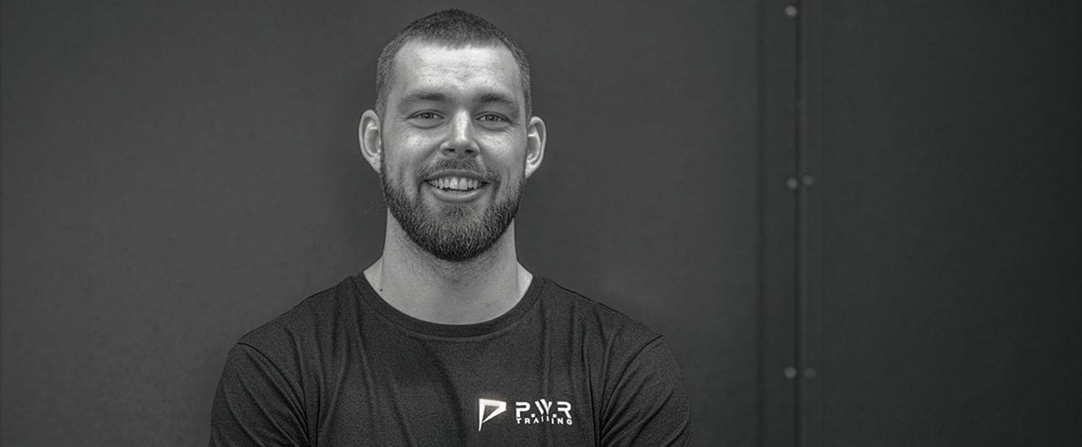 Philip Eriksson. En person i sportkläder står med armarna i kors och ler. Svartvitt porträtt.