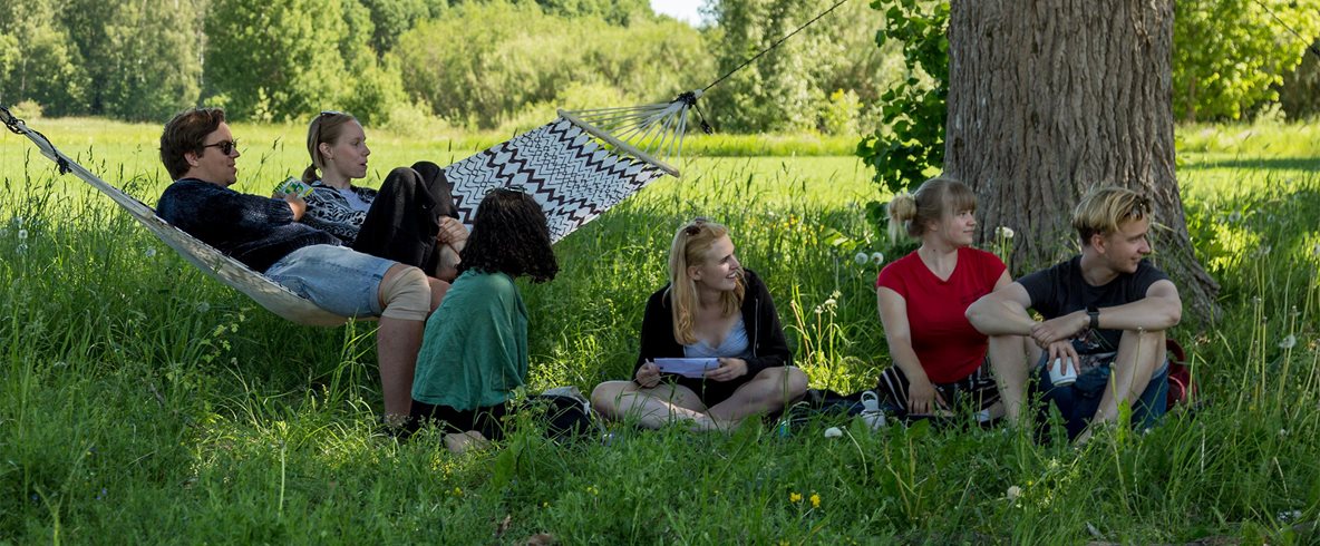 En grupp deltagare sitter i skuggan under träden på Kävesta folkhögskola.