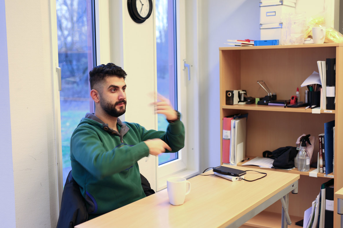 Ung man till vänster i bild tecknar till en person utanför bild till höger.