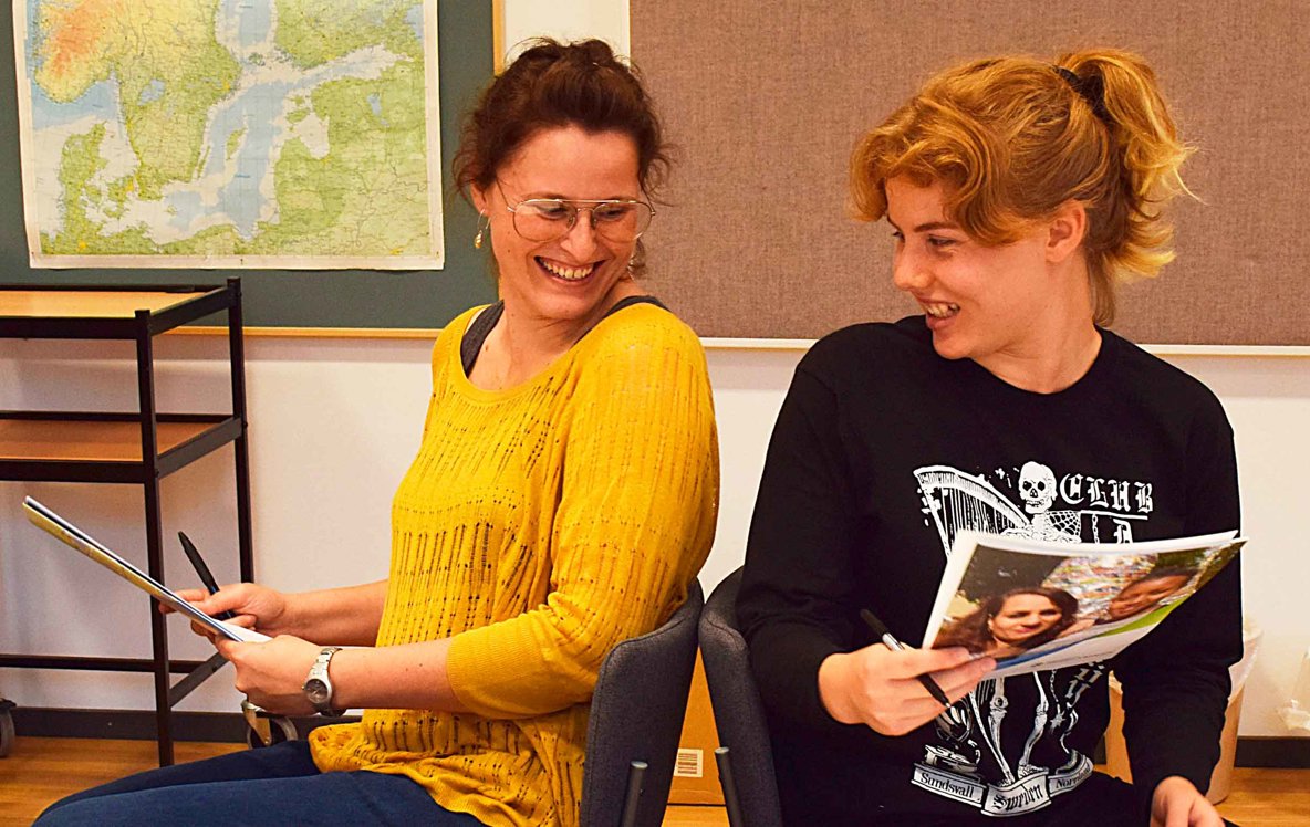 Två kvinnor sittande på var sin stol, tittar på varandra och ler.