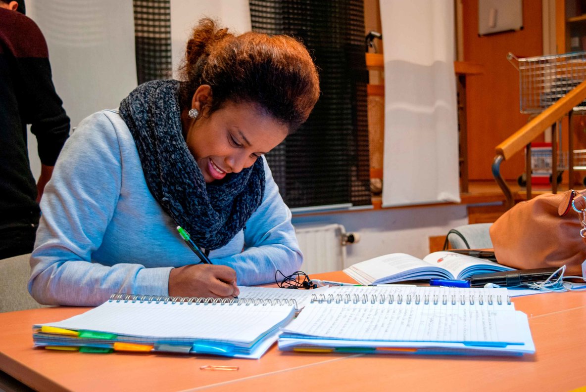 Glad kvinna sitter vid bord och pluggar.