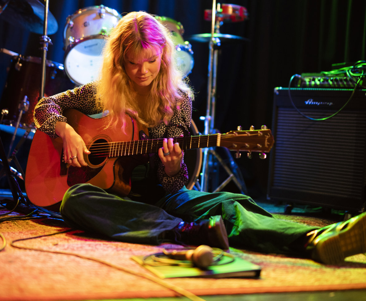 En person sitter ner och spelar gitarr. 