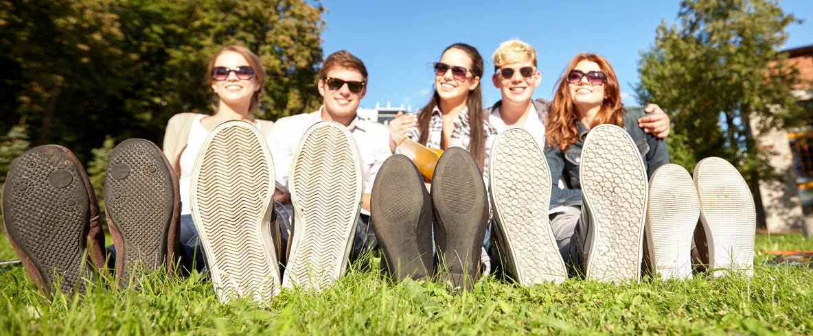 Fem unga personer sitter på en gräsmatta med skosulorna riktade mot kameran.