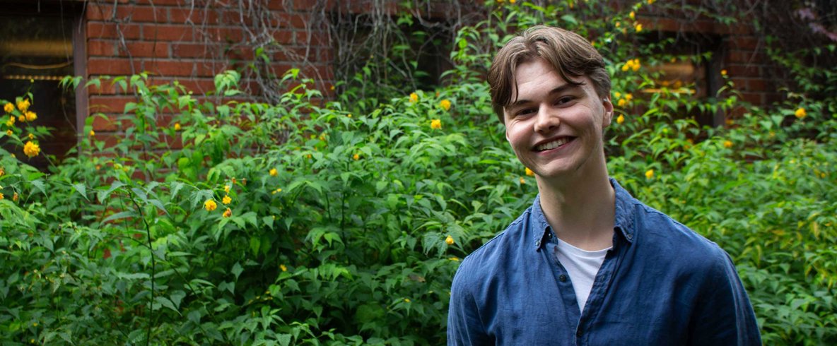 En person står vid en buske och ler mot kameran.