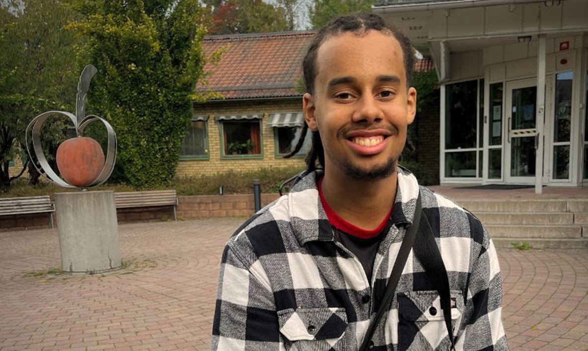 En person tittar in i kameran. I bakgrunden syns en skulptur av ett äpple.