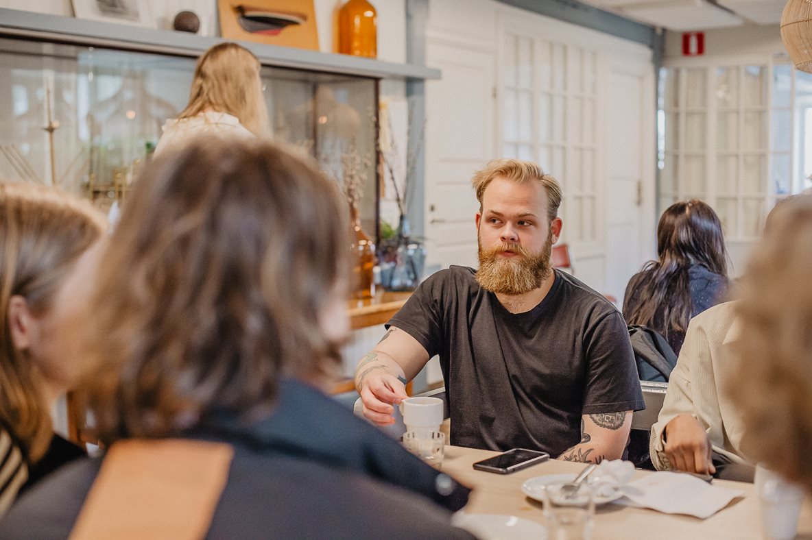 En man, blond och med skägg, sitter vid ett bord och håller i en kaffemugg.