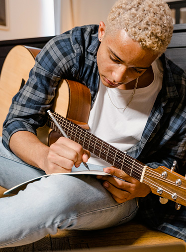 Bild: Ung man med gitarr skriver p&aring; ett papper.
