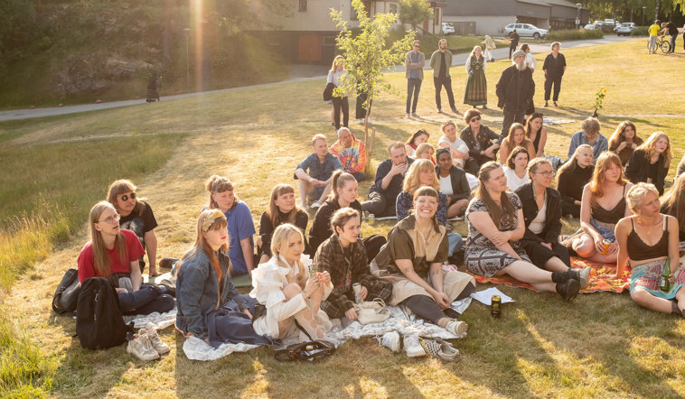 En flock glada deltagare sitter på en gräsmatta