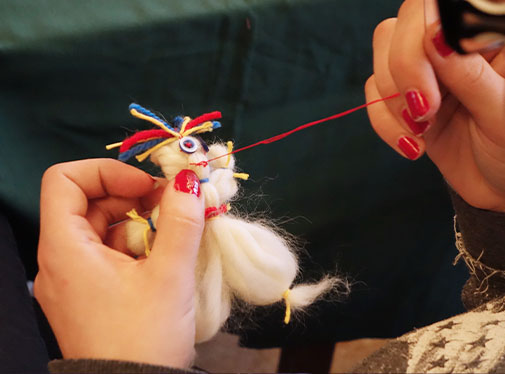 Bild: Närbild på händer som syr fast detaljer på en liten figur av garn.