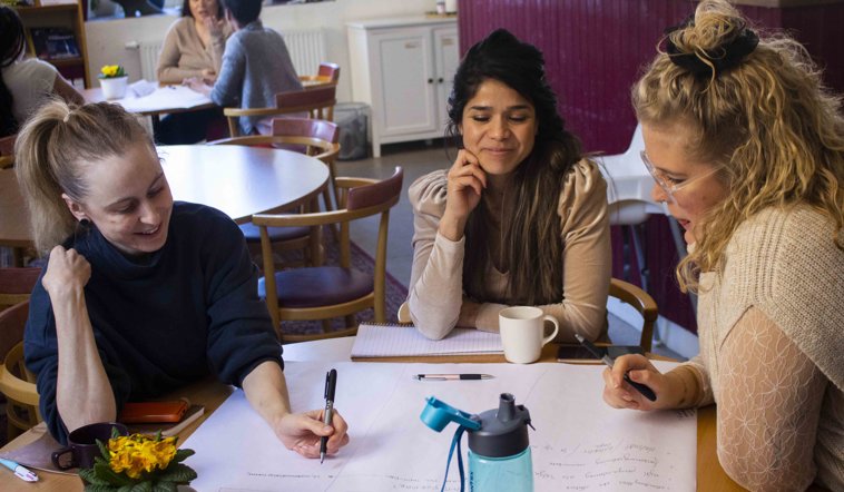 Tre personer sitter runt ett bord och diskuterar