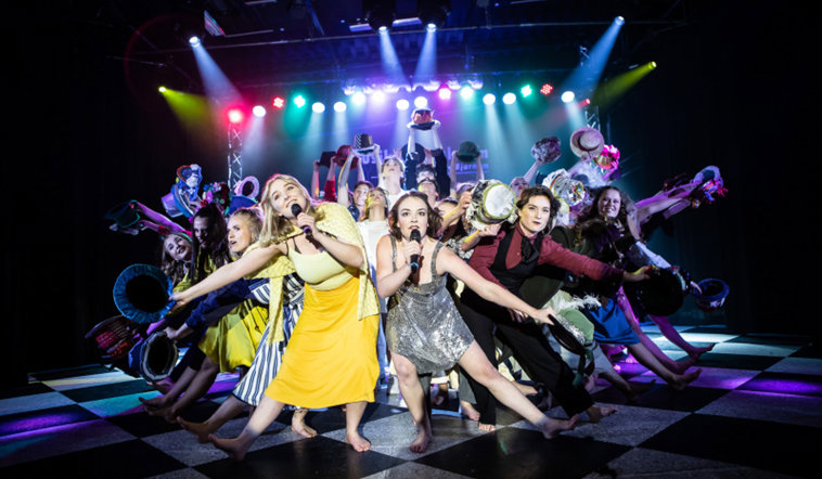 En scenshow på Musikteaterskolan med samlad ensamble i kostym som sjunger och dansar.